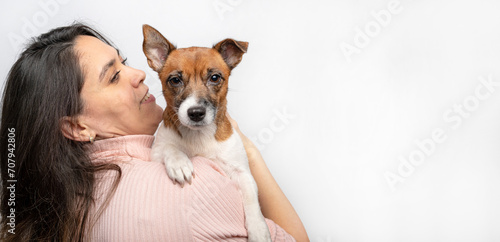 Photo of a joyful girl with dark hair wearing a sweater, feeling cheerful, holding a small Jack Russell Terrier puppy, expressing affection, good relationship, owner feeling responsible. Pedigree pets photo