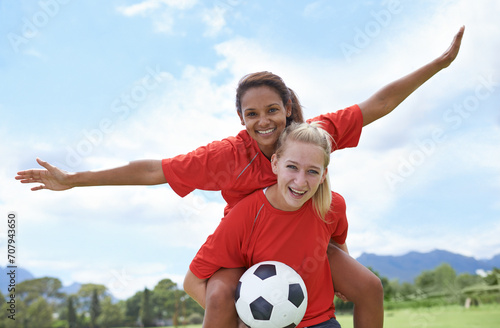 Happy woman, friends and piggyback for outdoor soccer on green grass in winning, achievement or sport in nature. Portrait of female person or football player smile for match, game or victory on field © Tasneem H/peopleimages.com