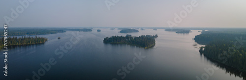 Aerial panoramic view of a large lake with many small islands. The lake is calm with small waves. The sky is filled with forest fire smoke creating a somber scene. 