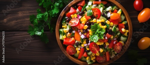 Colorful fresh vegetable salad with beans, corn, tomato, and bell pepper, served in a bowl with baked tortilla strips, photographed from above on wood (Selective Focus, Focus on the salad).