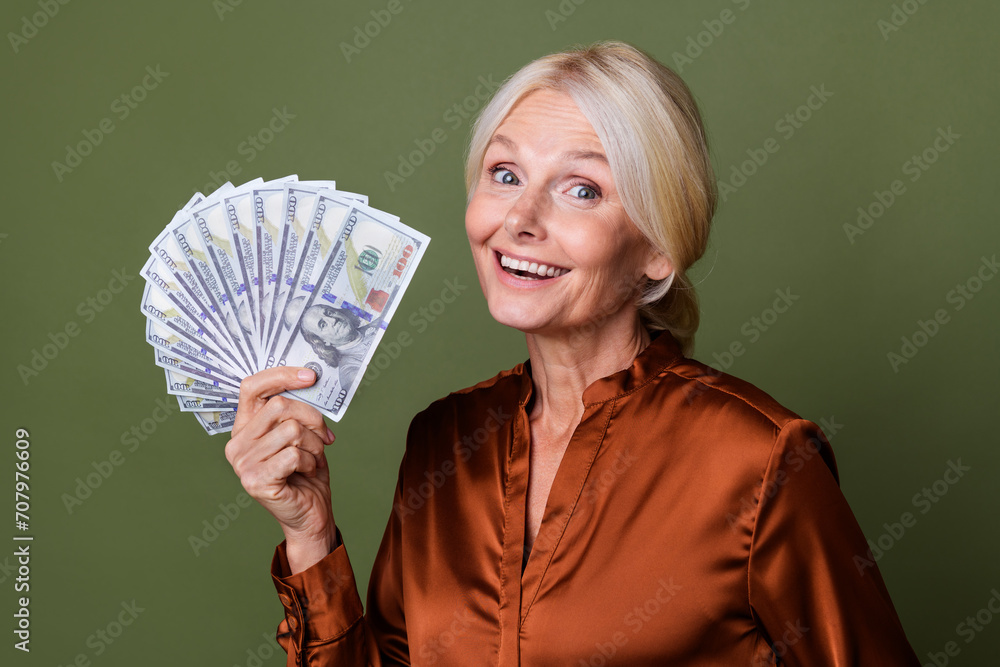 Photo of impressed satisfied woman with blond hair dressed silk shirt hold money astonished staring isolated on green color background Photo of impressed satisfied woman with blond hair dressed silk shirt hold money astonished staring isolated on green color background