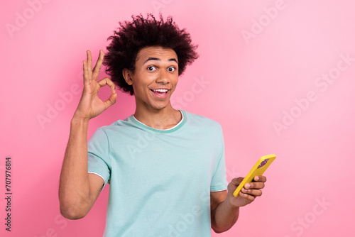 Photo of cool confident guy wear blue t-shirt texting apple samsung iphone device showing okey isolated pink color background