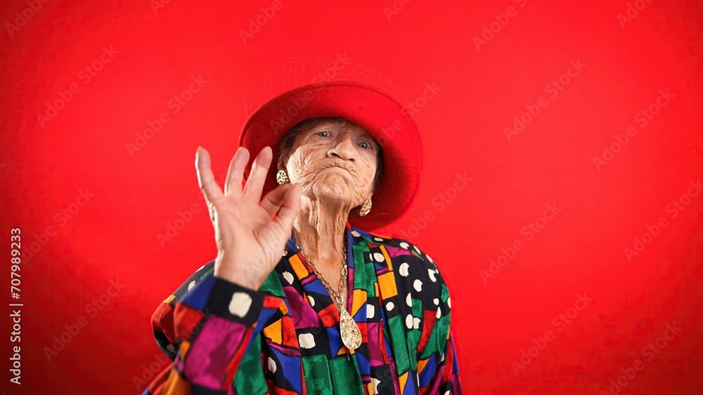 Funny portrait of mature elderly woman, 80s, having giving OKAY gesture, wearing red hat isolated on red background. Funny portrait of mature elderly woman, 80s, having giving OKAY gesture, wearing red hat isolated on red background.