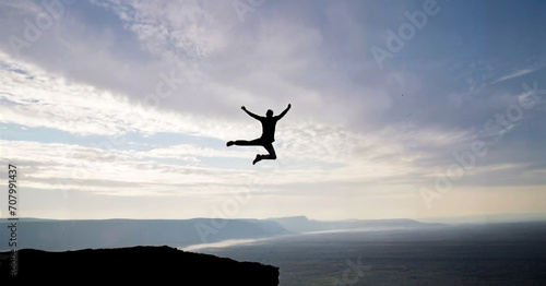 Silhouette of a Man jump and rises arms up on a peak. The happiness and success concept