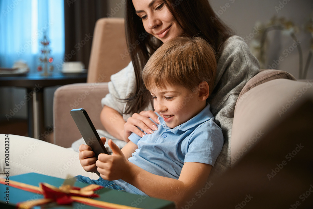 Little boy watching cartoons online on smartphone while sitting with mother Little boy watching cartoons online on smartphone while sitting with mother