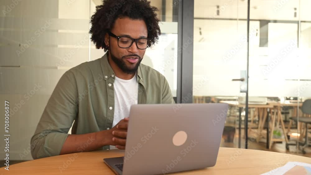 Male office employee greeting participant of virtual meeting. African-American millennial man using laptop for video call, chatting with coworkers or customers online on the distance Male office employee greeting participant of virtual meeting. African-American millennial man using laptop for video call, chatting with coworkers or customers online on the distance