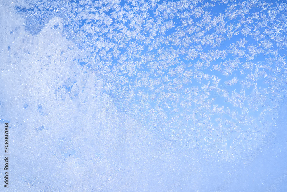 Abstract winter background. Frost on a frozen window against the blue sky.