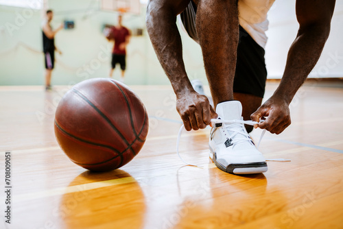 Young man tying sneakers next to basketball in gym photo
