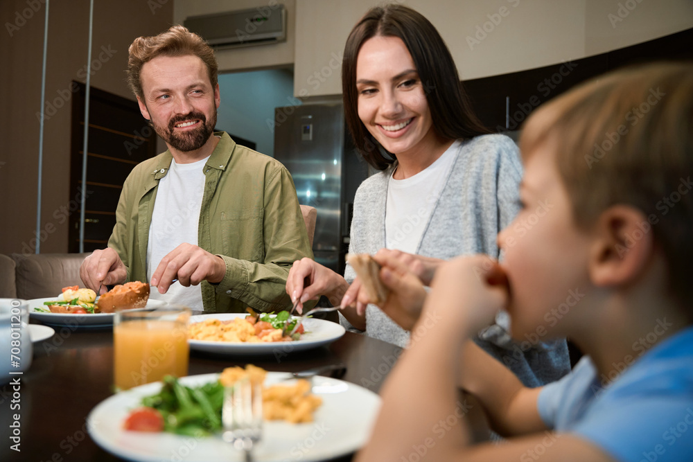 Couple looking at their son with smiles while having festive breakfast in hotel Couple looking at their son with smiles while having festive breakfast in hotel