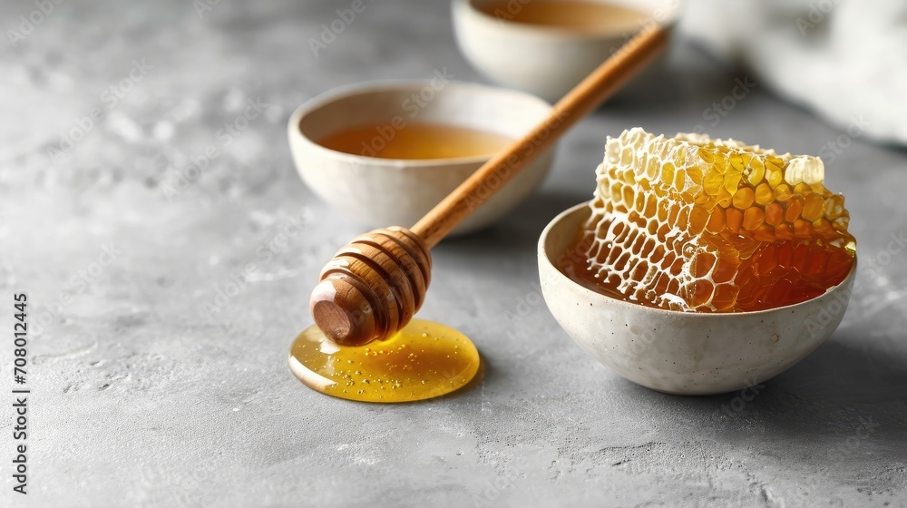 Fototapeta premium minimalist setting with a bowl of honey, a honey comb and a wooden dipper on a gray background