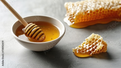 minimalist setting with a bowl of honey, a honey comb and a wooden dipper on a gray background