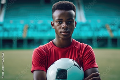 Athletic studio portrait of a young African man as a soccer player, with a football, isolated on a stadium background