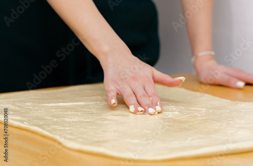 One Caucasian young girl greases the dough on the table with butter.