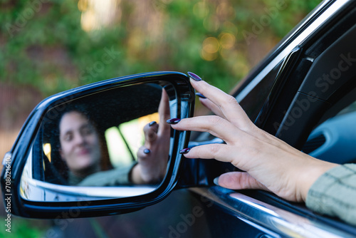 Hand of woman driver adjusting the side view mirror of her car. Selective focus. Transportation, travel and road safety concepts photo