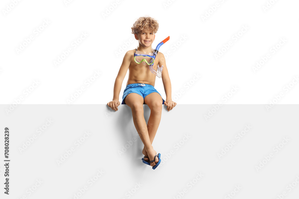 Boy in swimming shorts and a diving mask sitting on a blank panel Boy in swimming shorts and a diving mask sitting on a blank panel
