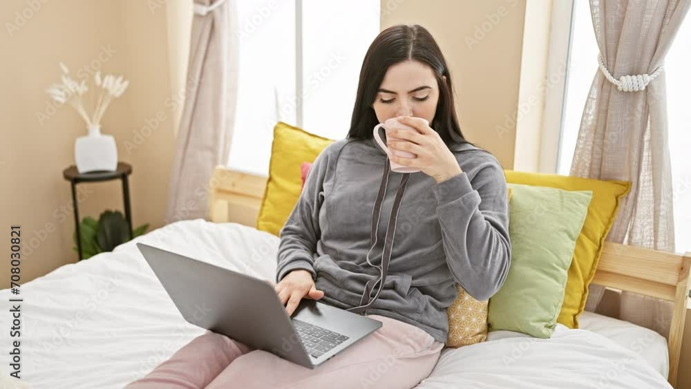 Hispanic woman drinking coffee and using laptop in a cozy bedroom setting Hispanic woman drinking coffee and using laptop in a cozy bedroom setting