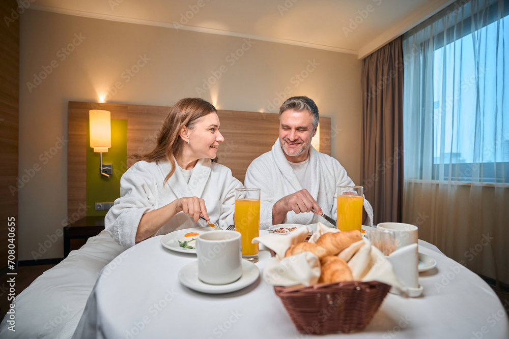 Smiling adult caucasian couple having breakfast on bed at table in hotel room Smiling adult caucasian couple having breakfast on bed at table in hotel room