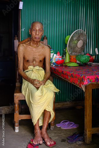 Bangladeshi rural elderly person sitting on a chair inside his home  photo