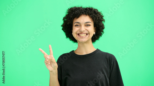 A woman, close-up, on a green background, shows a victory sign