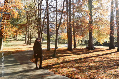 Fototapeta Naklejka Na Ścianę i Meble -  Woman enjoying a beautiful autumn day in the park with golden foliage and long shadows.