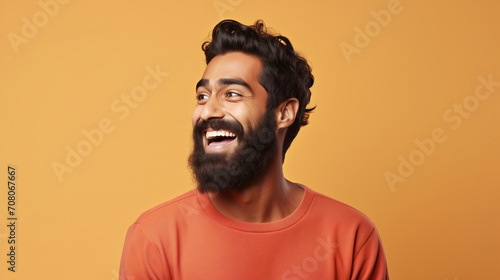 An Indian man with a beard and broad smile exudes a sense of joy and carefree spirit, set against a monochromatic orange background that accentuates the subject's infectious enthusiasm © SkyLine
