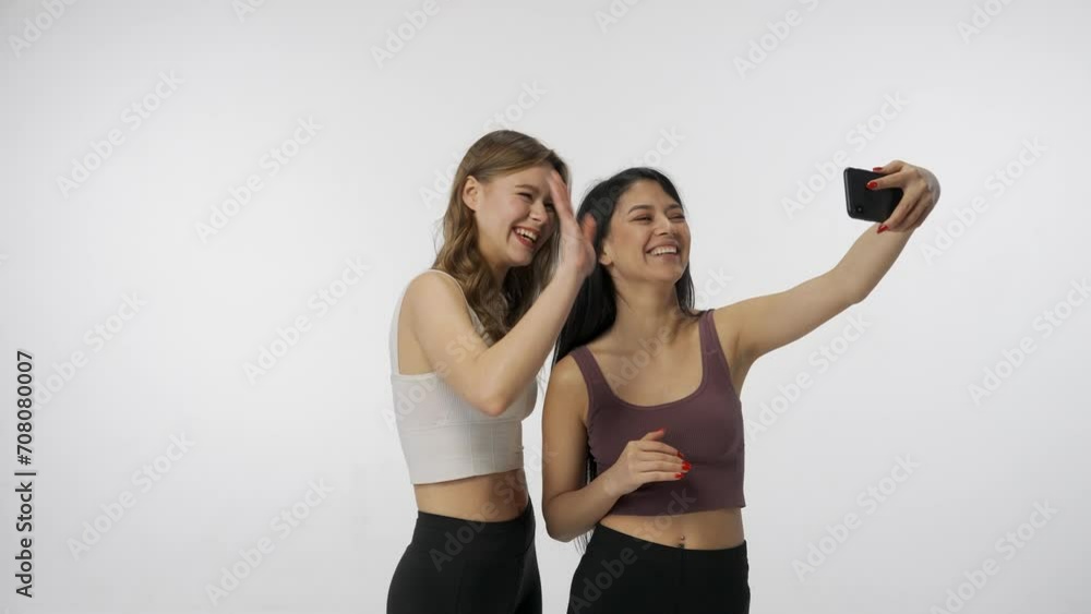 Portrait of young multiracial models isolated on white background. Group of two attractive multiethnic girls taking selfie video on smartphone. Multiethnic beauty concept. Portrait of young multiracial models isolated on white background. Group of two attractive multiethnic girls taking selfie video on smartphone. Multiethnic beauty concept.