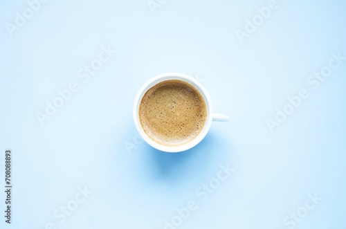 On a blue background there is a white cup with hot, aromatic, delicious cappuccino coffee. Flat lay, top view, close-up. Concept coffee break, hot drinks. Space for copying text.