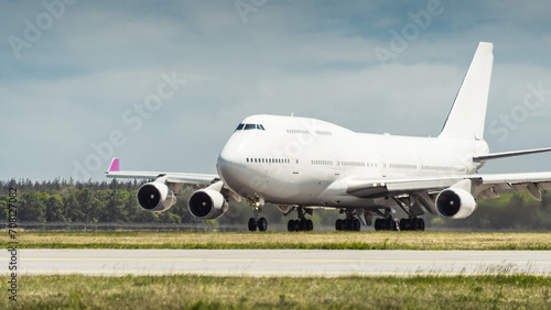 Huge white passenger aircraft accelerating for take-off along the runway, hot exhaust coming out of the engine and distorts the visibility. Front three quarter view of two-storey jumbo jet on a ground