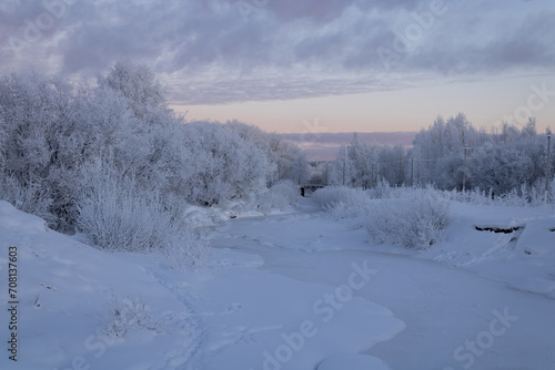 Panorama of a frozen river and snow-covered trees in a winter park. Sunset, polar night. A city in the Far North of Russia.
