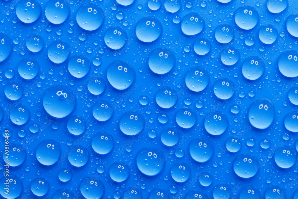 closeup, macro of many water drops, droplets, on a blue surface, background, a pair of eyes that are reflected in every drop