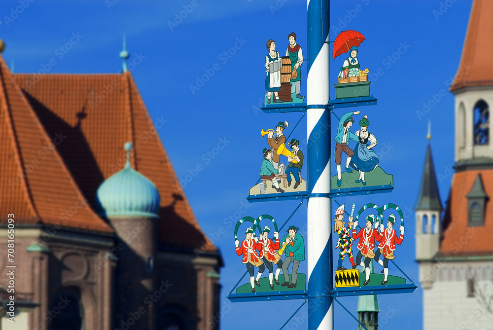 Fototapeta premium Maypole on Viktualienmarkt with musicians, dancing couple, market woman, waitress of Oktoberfest, tower of new town hall in background, Munich, Bavaria, Germany, Europe