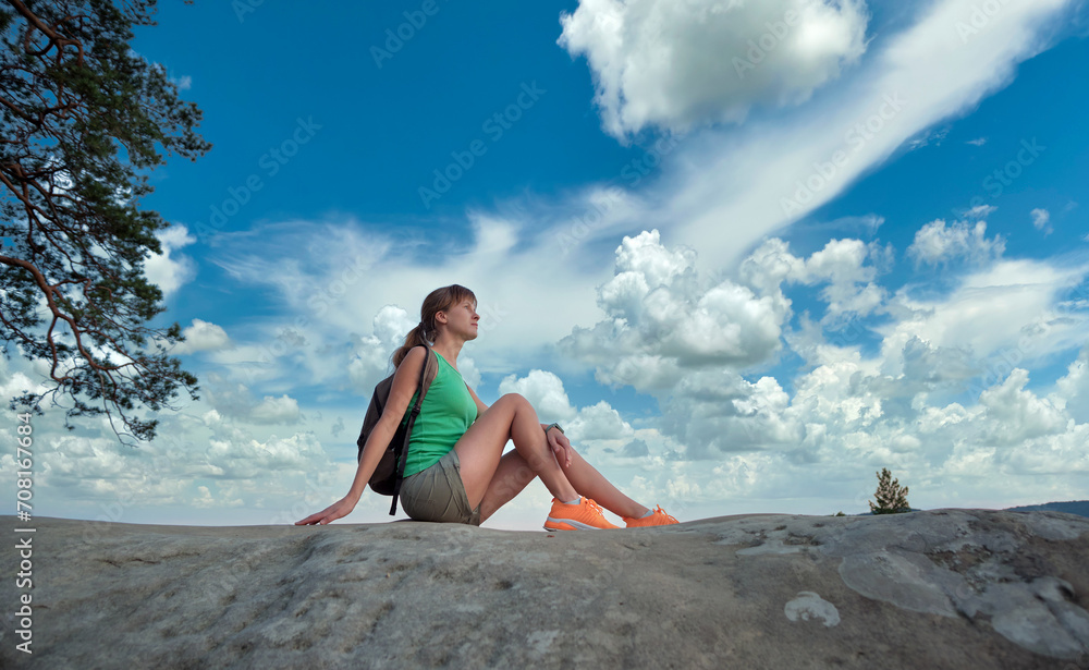 Woman hiker seated alone on rocky mountain cliff enjoying view of nature on wilderness trail. Active way of life concept