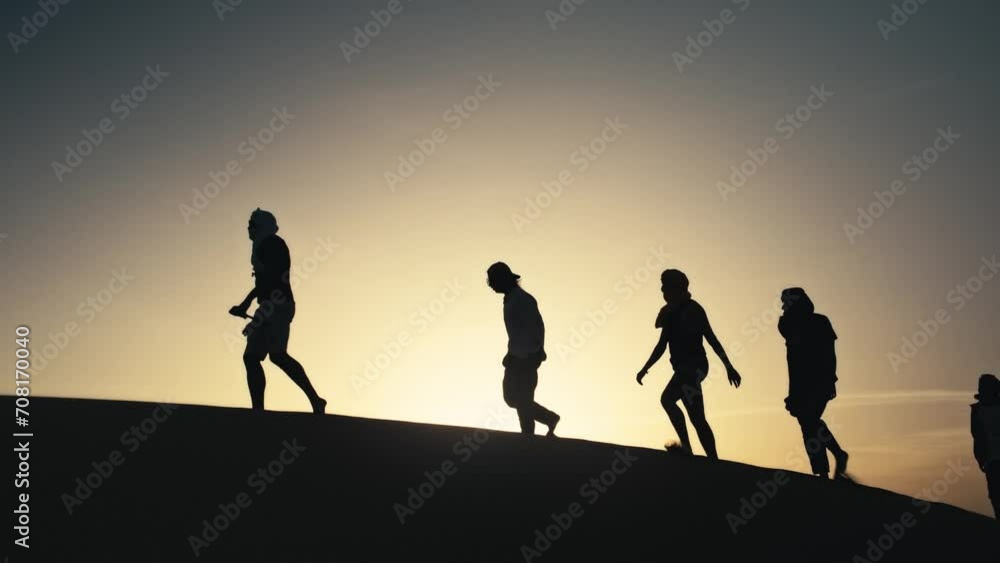 silhouettes of a group of people crossing and walking on a sand dune in the sahara desert in morocco at sunset silhouettes of a group of people crossing and walking on a sand dune in the sahara desert in morocco at sunset