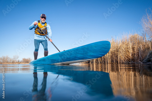 senior male paddler is paddling  a stand up paddleboard on a calm lake in spring, frog perspective from an action camera at water level photo