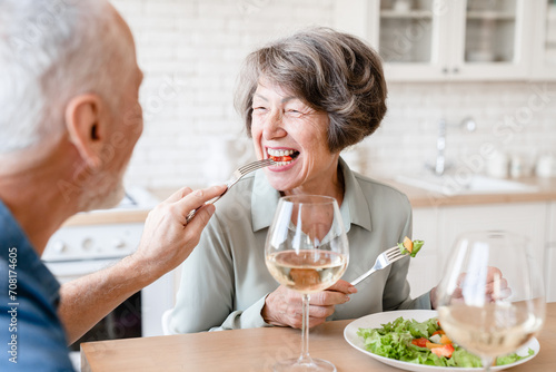 Quality time - love language. Old elderly senior caucasian family couple grandparents spouses treating each other while eating, celebrating anniversary on romantic date dinner at home kitchen