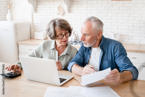 Busy caucasian old elderly senior couple making calculations at home kitchen, checking the document, revising data, information, counting domestic bills and rentals photo