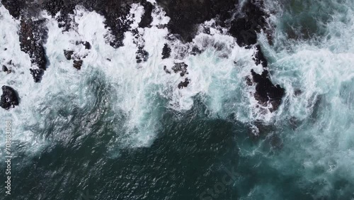 Overhead view captured by drone of violent ocean waves crashing on the shore of a Hawaii beach on the island of Kauai during a storm. The whitecap sea water is exploding on the rocky shore.  photo