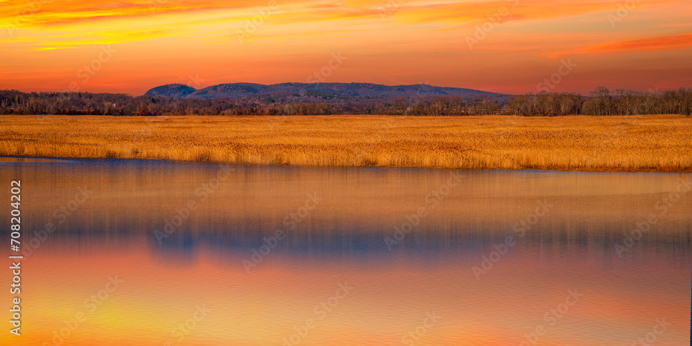 Dramatic Sunset over Sleeping Giant Mountain, Gold-colored Common Reeds Plants, and the Quinnipiac River in Hamden viewed from Tidal Marsh Trail in North Haven, Connecticut
