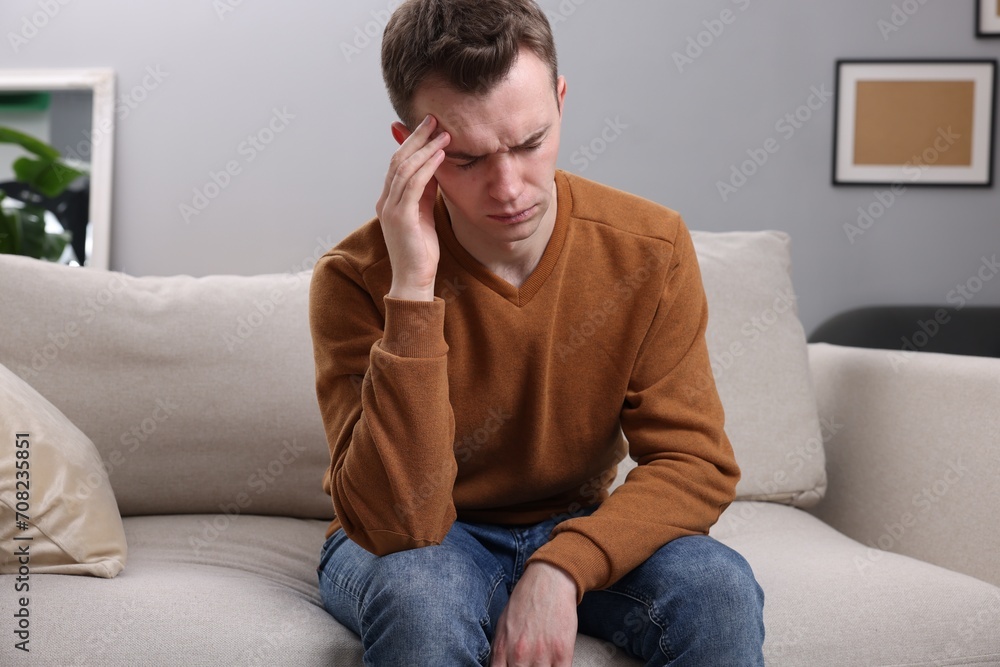 Sad man suffering from headache on sofa indoors Sad man suffering from headache on sofa indoors