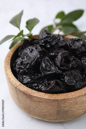 Sweet dried prunes in bowl on white table, closeup