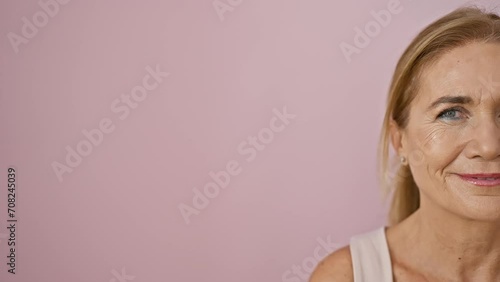 Portrait of a smiling middle-aged woman with blonde hair against a pink wall, capturing her mature beauty and poise. photo