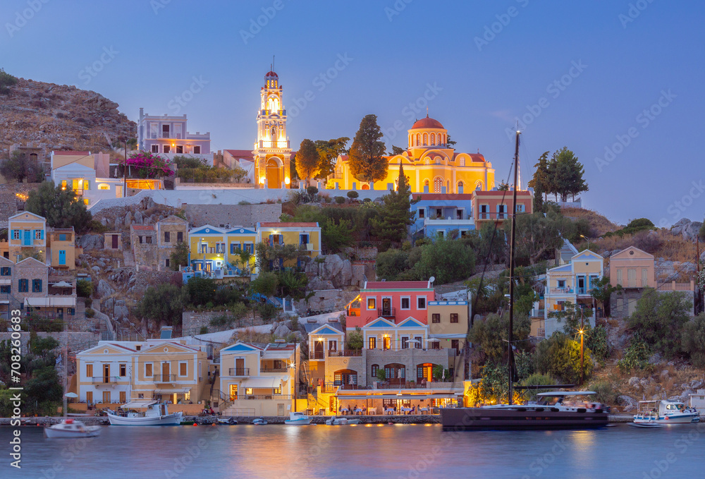 Fototapeta premium Multi-colored facades of houses in the light of lanterns in the village of Symi at sunset.