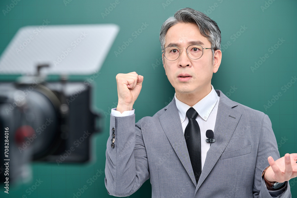 A middle-aged man is wearing a suit and giving a lecture in front of the camera pointing to the blackboard. A middle-aged man is wearing a suit and giving a lecture in front of the camera pointing to the blackboard.