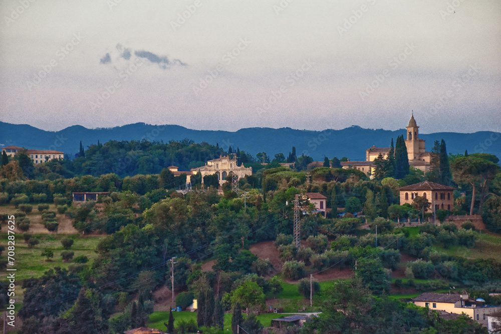 Tuscany rolling hills from Siena, rural misty evening landscape. Green farm fields with cypress trees. Italy 2023