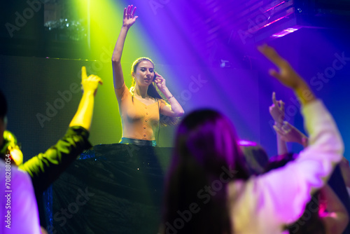 Caucasian female DJ with Turntables at nightclub. Group of diverse young people dancing in night club. Nightlife and disco dance party concept. Fun music festival
