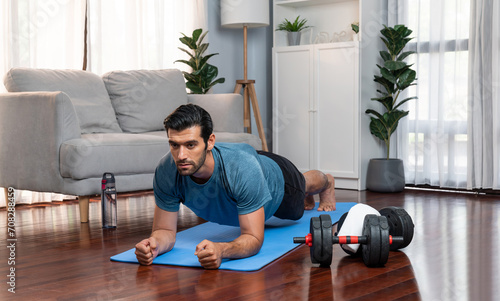 Athletic and sporty man doing plank on fitness mat during home body workout exercise session for fit physique and healthy sport lifestyle at home. Gaiety home exercise workout training.