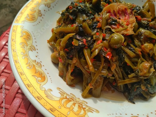 Stir-fried spicy kale with strong spices mixed with cempoka and tepus flowers served on a plate photo