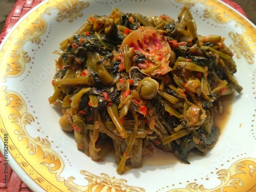Stir-fried spicy kale with strong spices mixed with cempoka and tepus flowers served on a plate photo