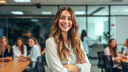 Young smiling successful businesswoman in formal wear standing in boardroom with arms crossed and looking at camera.In background her colleagues having meeting. Free Download Young smiling successful businesswoman in formal wear standing in boardroom with arms crossed and looking at camera.In background her colleagues having meeting. - GFXLoad