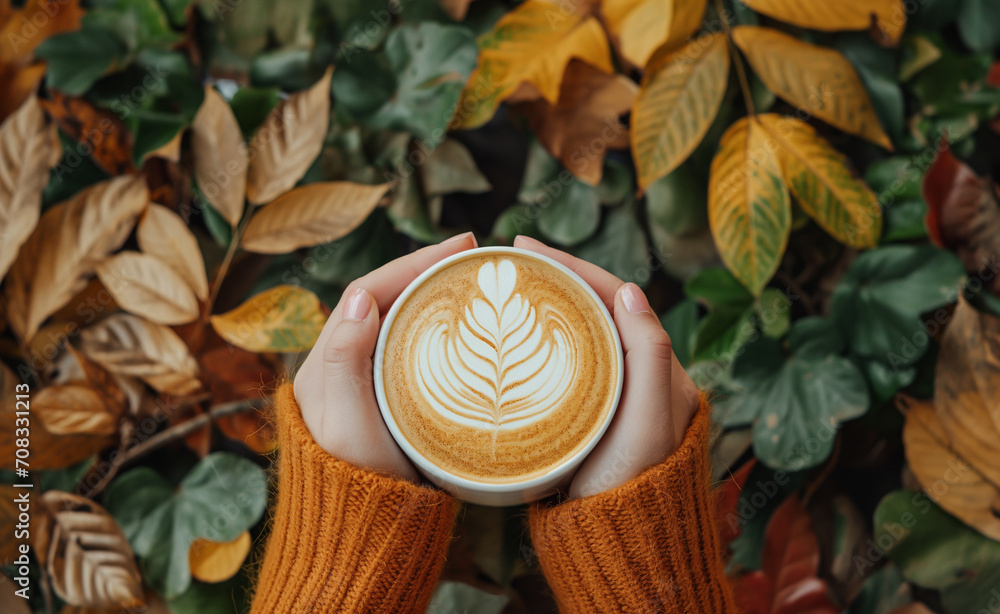 Top view of woman hands holding coffee with latte art on seasonal autumn leaves background. Top view of woman hands holding coffee with latte art on seasonal autumn leaves background.